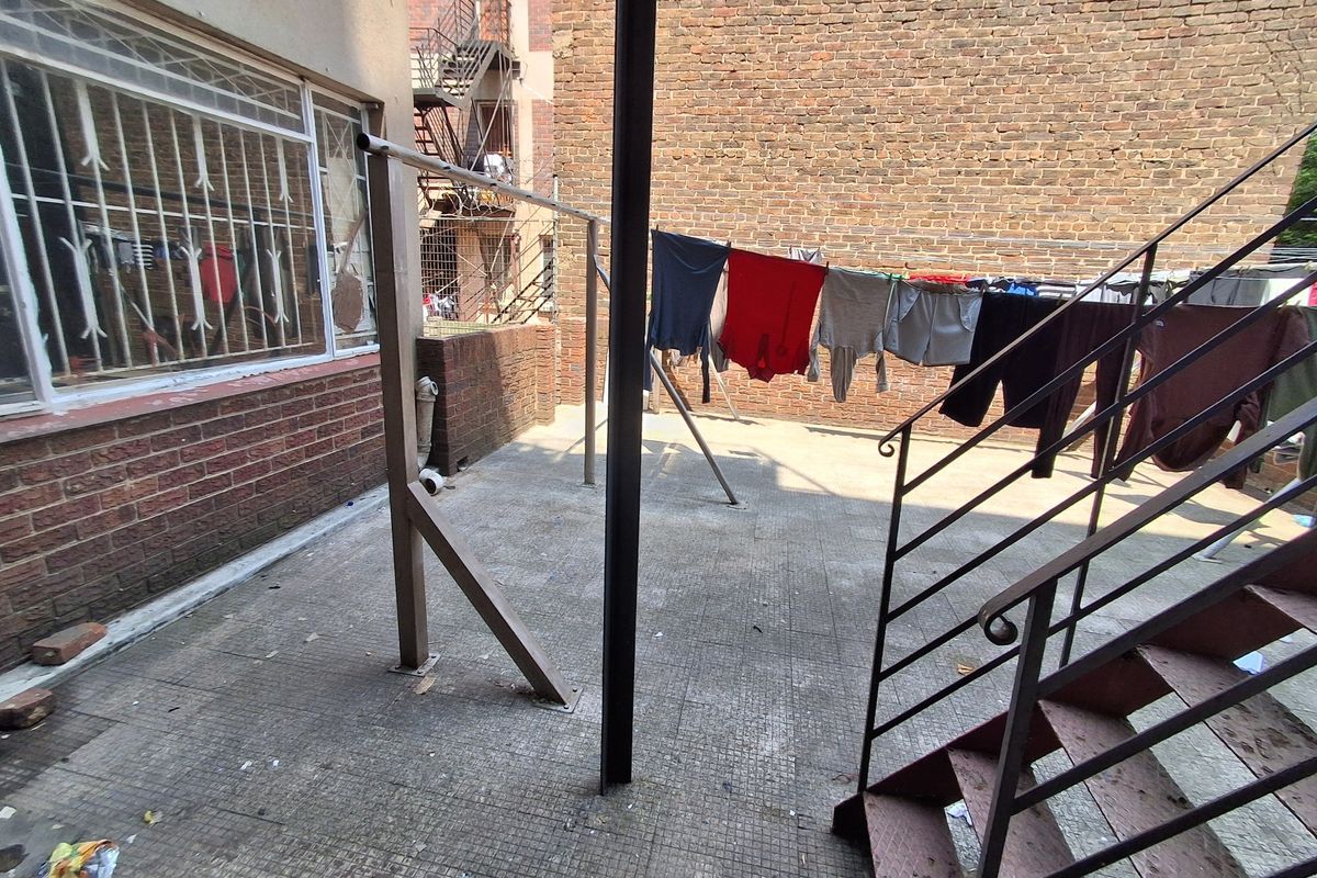 A rear exterior courtyard area featuring a paved patio, metal staircase, and brick boundary walls, providing functional outdoor space for the apartment.