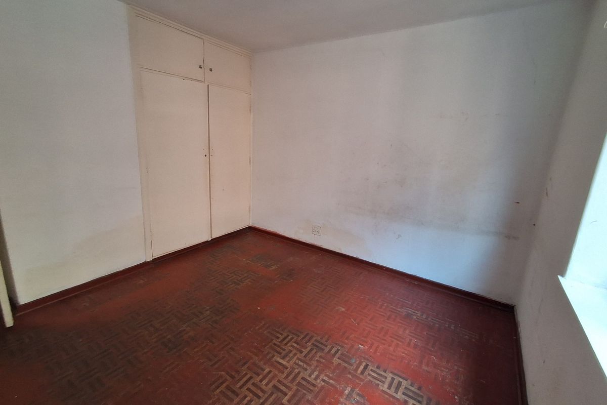 An empty bedroom featuring original parquet flooring and built-in cupboards, requiring cosmetic updates and wall repairs to restore its appeal.