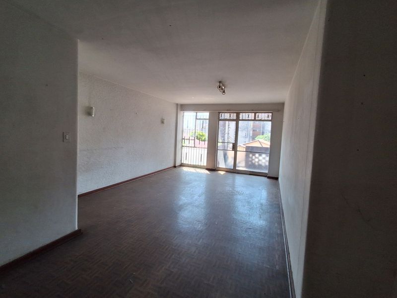 An empty, spacious living area featuring parquet flooring, wall sconces, and a sliding glass door with security gate leading to an outdoor space.