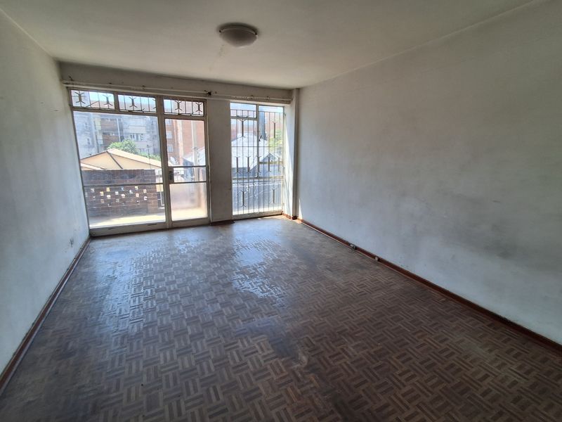An empty living room featuring original parquet flooring, large windows with security bars, and access to a small balcony area.