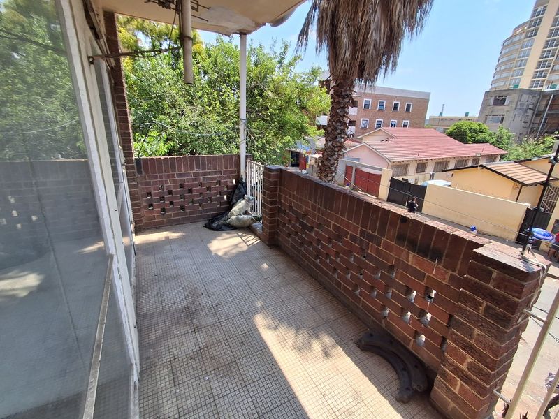 An open-air balcony featuring a brick balustrade and tiled flooring, offering an elevated view of the surrounding neighborhood.