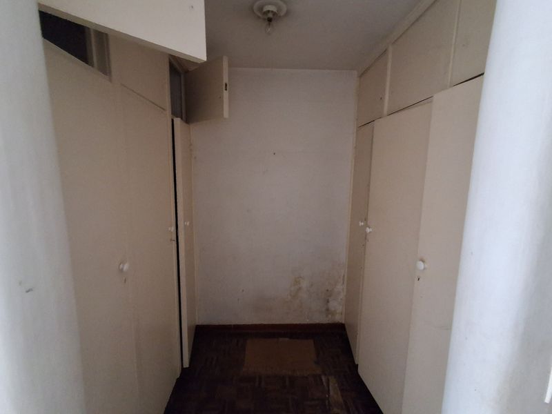 A narrow hallway featuring built-in storage cupboards and parquet flooring, showing signs of wall staining and wear.