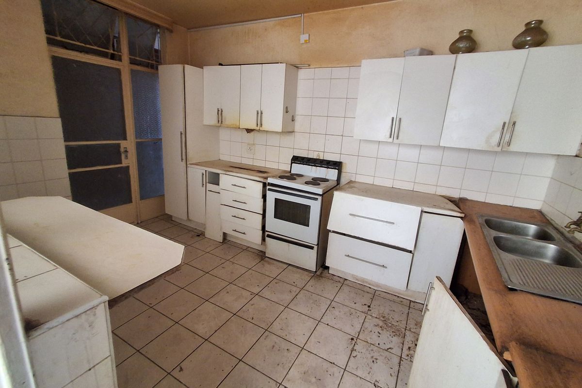 A dated kitchen featuring original cabinetry, a freestanding stove, and a double sink, requiring significant renovation and cosmetic updates to restore functionality.