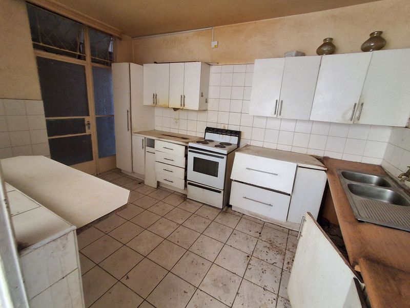 A dated kitchen featuring original cabinetry, a freestanding stove, and a double sink, requiring significant renovation and cosmetic updates to restore functionality.