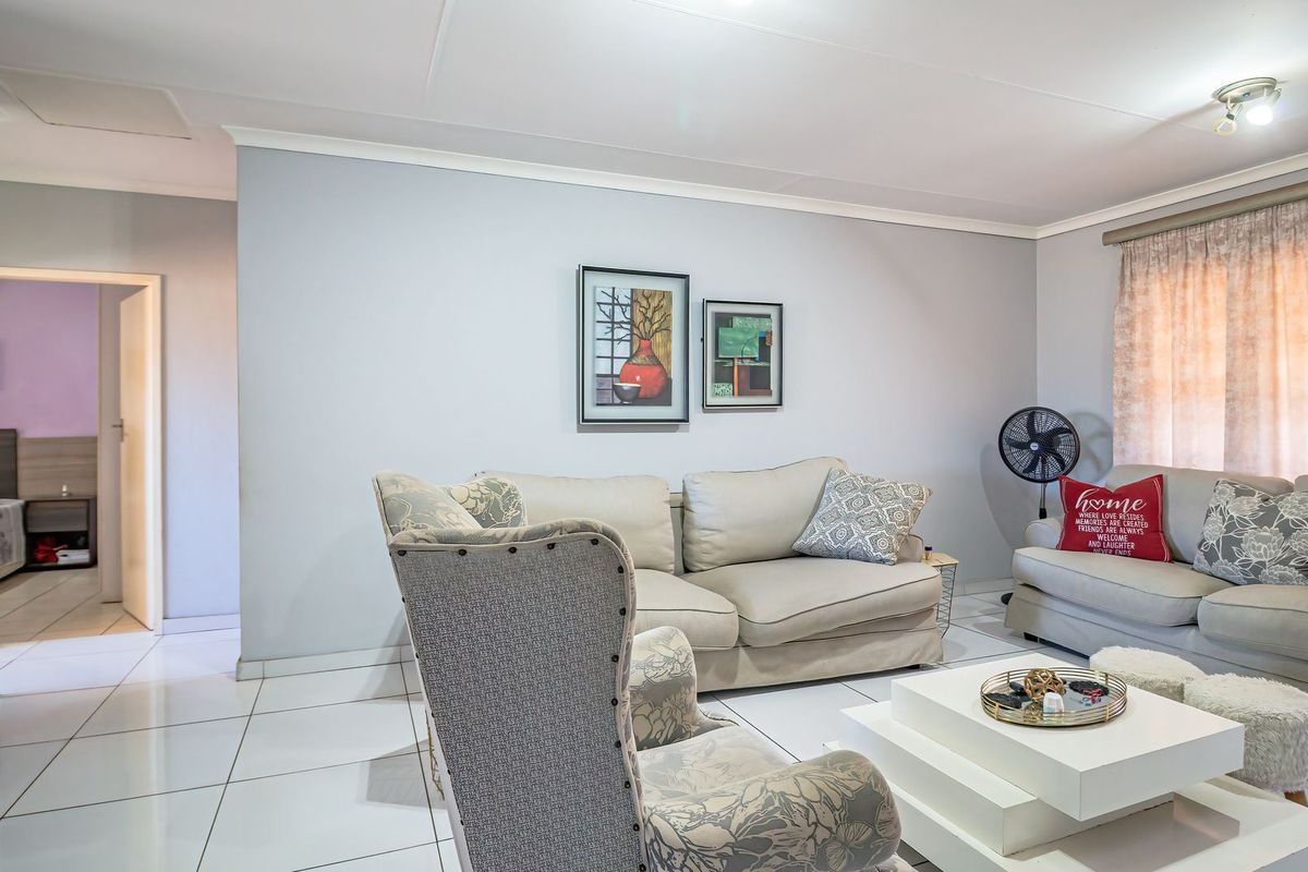 A well-maintained living room featuring neutral tiled flooring, light grey walls, and a built-in cupboard, offering a clean and functional living space.