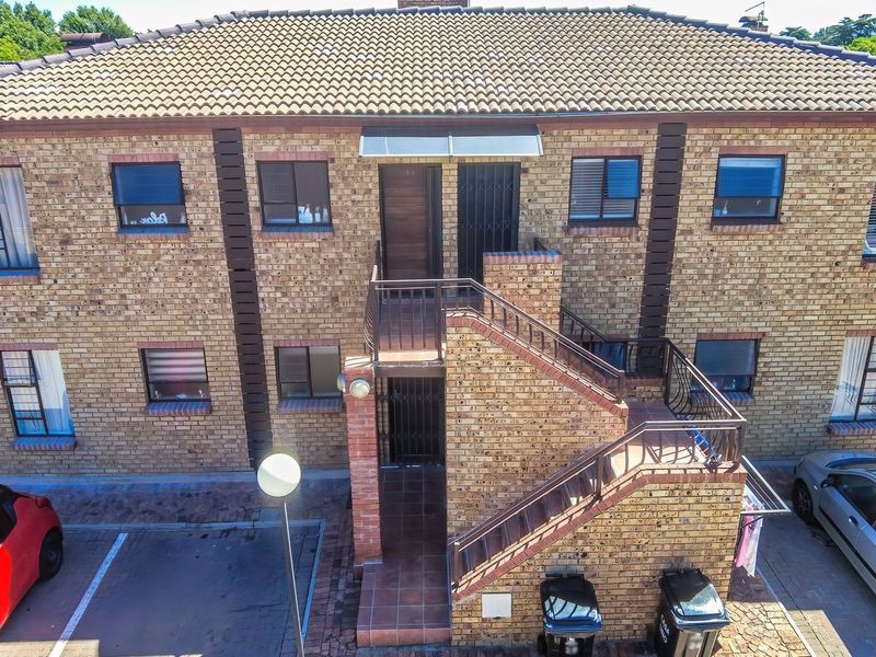 Front elevation of a two-story face brick apartment building featuring an external staircase, security gates, and dedicated paved parking bays.