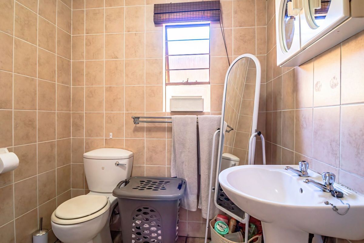 A functional bathroom featuring a pedestal basin, toilet, and floor-to-ceiling tiled walls with a window for natural light.
