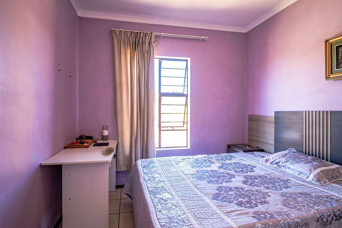 A bedroom featuring tiled flooring, a built-in headboard, and a louvered window, providing a functional space with potential for cosmetic updates.