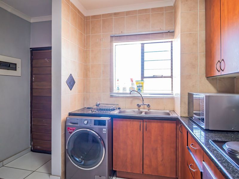 Functional kitchen featuring granite countertops, double sink, tiled splashback, and built-in wooden cabinetry with integrated hob and laundry appliance space.