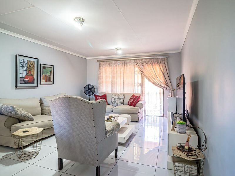 A bright and well-maintained living room featuring polished tiled flooring, neutral walls, and a sliding glass door providing access to an outdoor area.