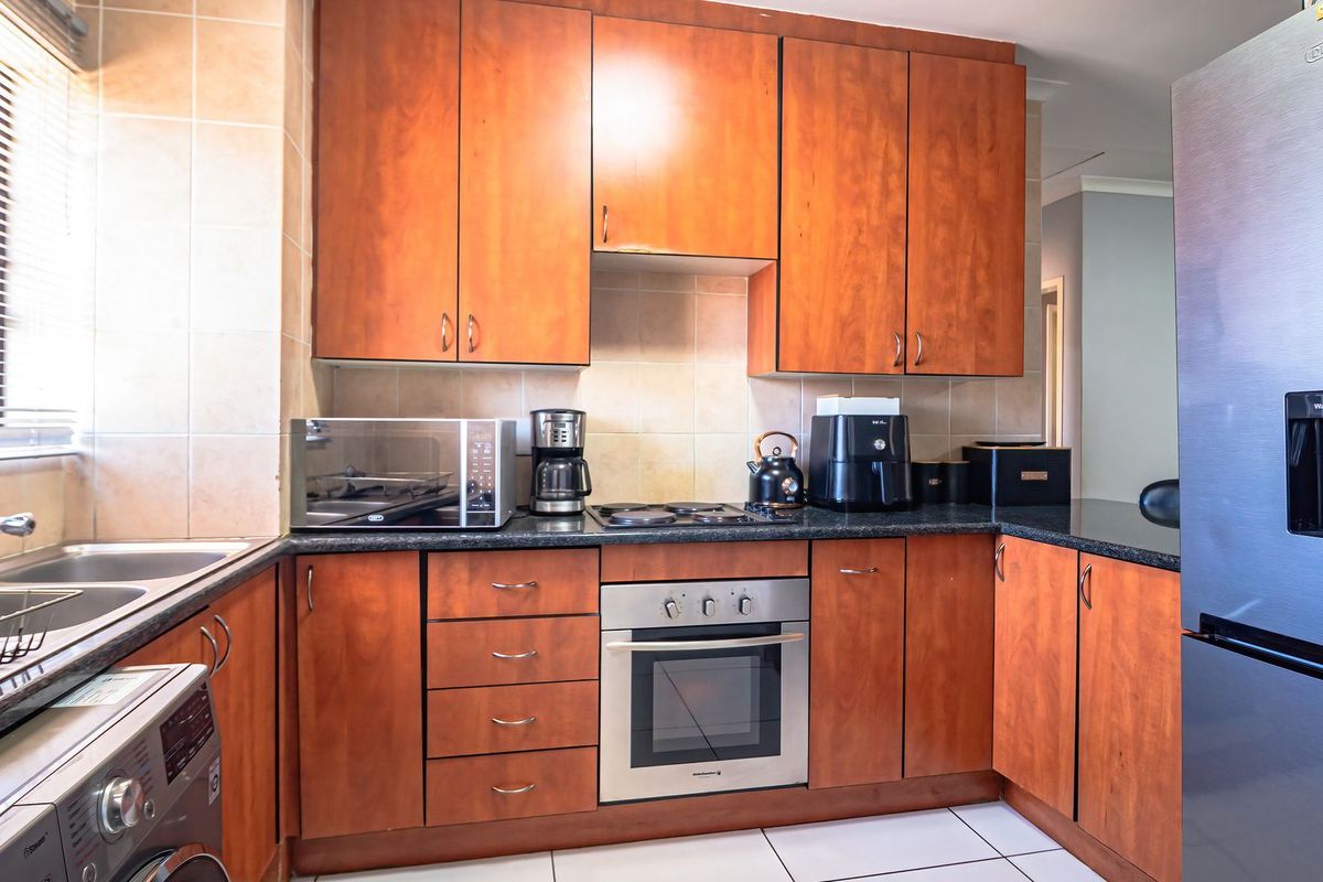 A functional kitchen featuring warm-toned wooden cabinetry, granite countertops, a built-in oven with electric hob, and a double basin sink with tiled backsplash.