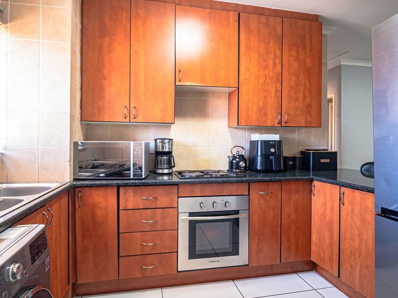A functional kitchen featuring warm-toned wooden cabinetry, granite countertops, a built-in oven with electric hob, and a double basin sink with tiled backsplash.