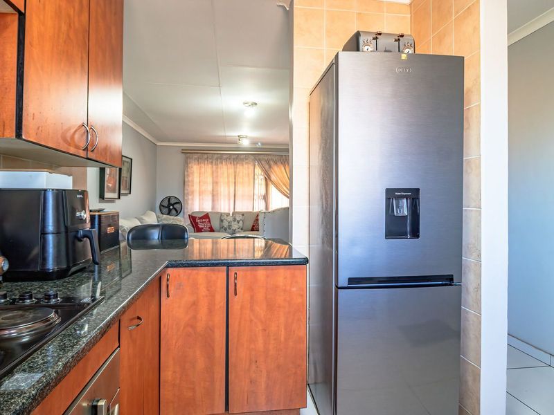 A functional kitchen featuring wooden cabinetry, granite countertops, and a tiled backsplash, with an open-plan layout flowing into the adjacent living area.