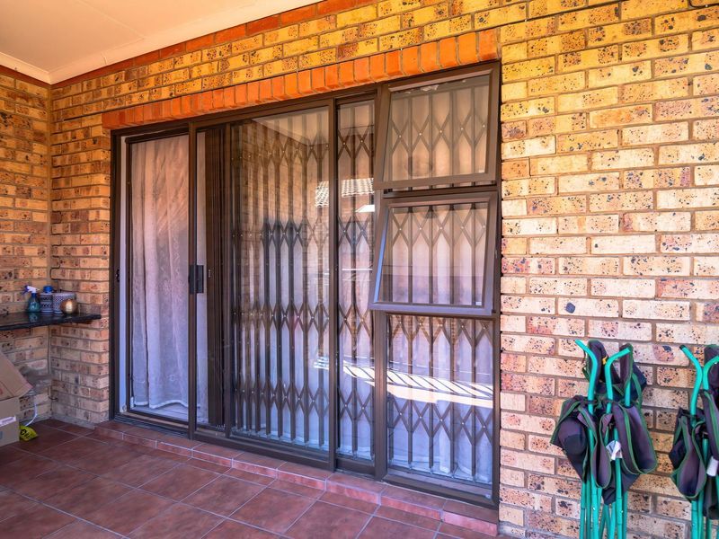 A covered patio area featuring face brick walls, tiled flooring, and a sliding glass door with integrated security gate.