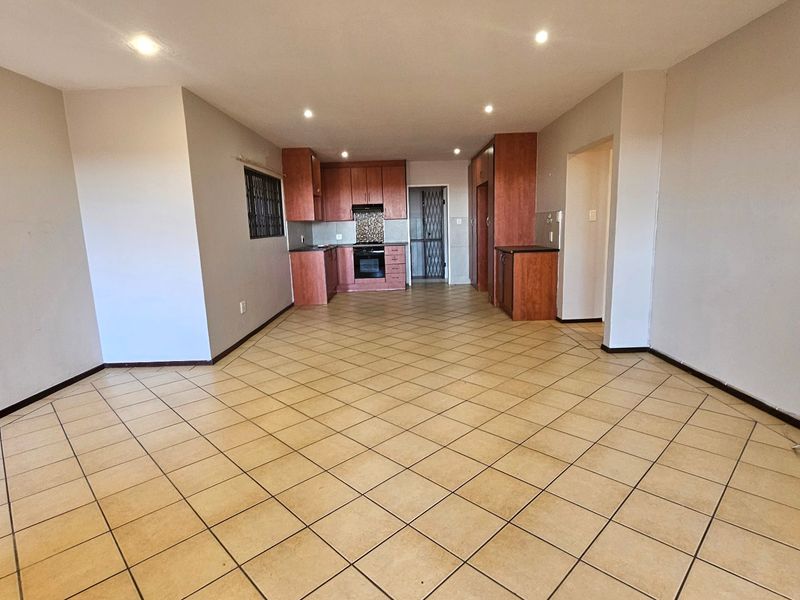 Spacious open-plan living area featuring tiled flooring, recessed lighting, and a functional kitchen with built-in cabinetry, oven, and hob.