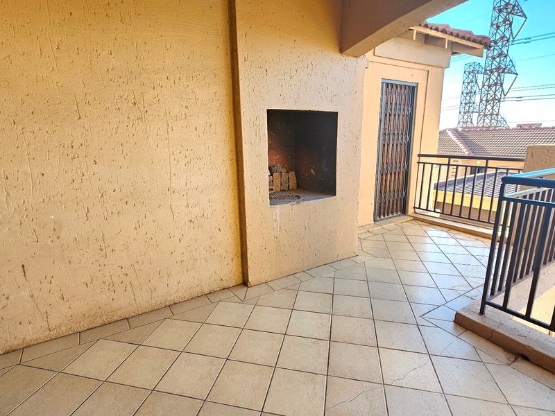 A covered balcony featuring tiled flooring, a built-in braai, and a metal security gate, offering an outdoor space for relaxation.