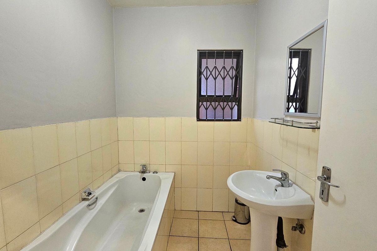 A functional bathroom featuring a bathtub, pedestal basin, and tiled finishes, equipped with a security-gated window for added safety.