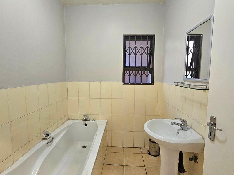 A functional bathroom featuring a bathtub, pedestal basin, and tiled finishes, equipped with a security-gated window for added safety.