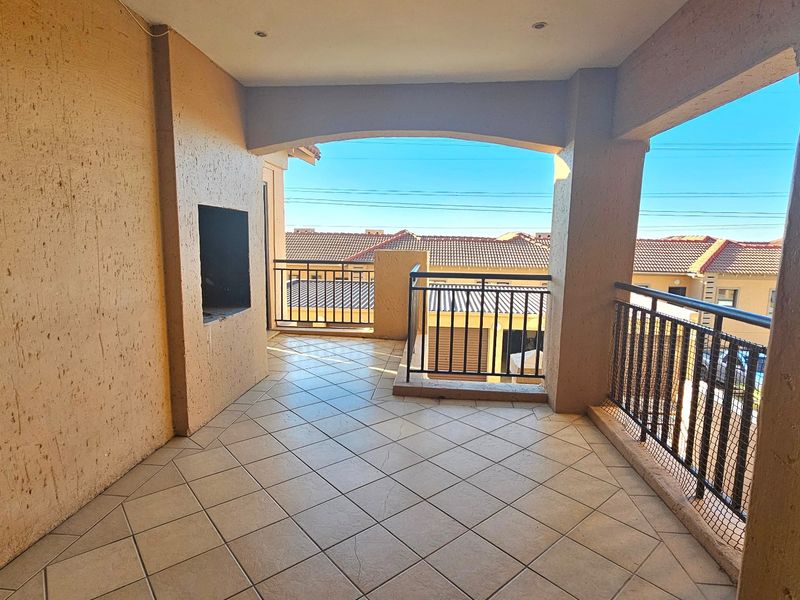 Spacious covered balcony featuring tiled flooring, a built-in braai, and metal balustrades, offering an ideal outdoor space for entertaining.