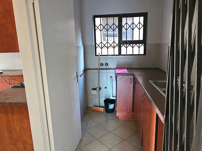 A functional scullery area featuring built-in cabinetry, a stainless steel sink, and tiled flooring, providing a practical space for laundry or additional kitchen prep.