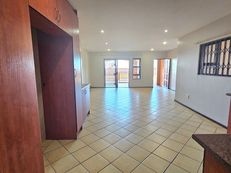Spacious open-plan living and kitchen area featuring tiled flooring, recessed lighting, and built-in cabinetry with granite countertops, leading to an outdoor balcony.