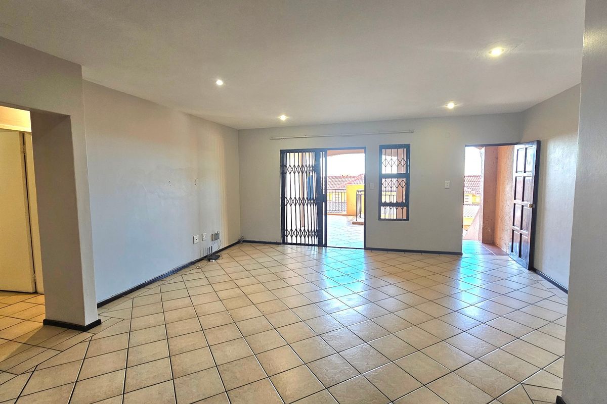 Spacious open-plan living area featuring neutral tiled flooring, recessed lighting, and direct access to an outdoor balcony through a secure sliding door.