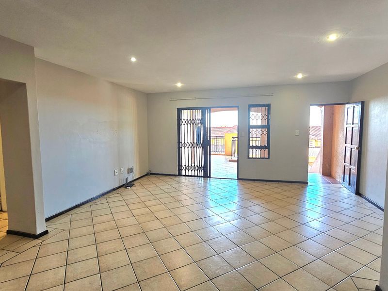 Spacious open-plan living area featuring neutral tiled flooring, recessed lighting, and direct access to an outdoor balcony through a secure sliding door.