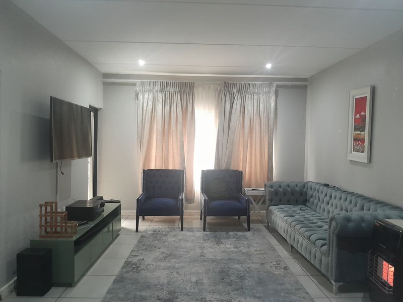 A well-maintained living room featuring neutral tiled flooring, recessed downlighting, and large window treatments, providing a comfortable and functional space.