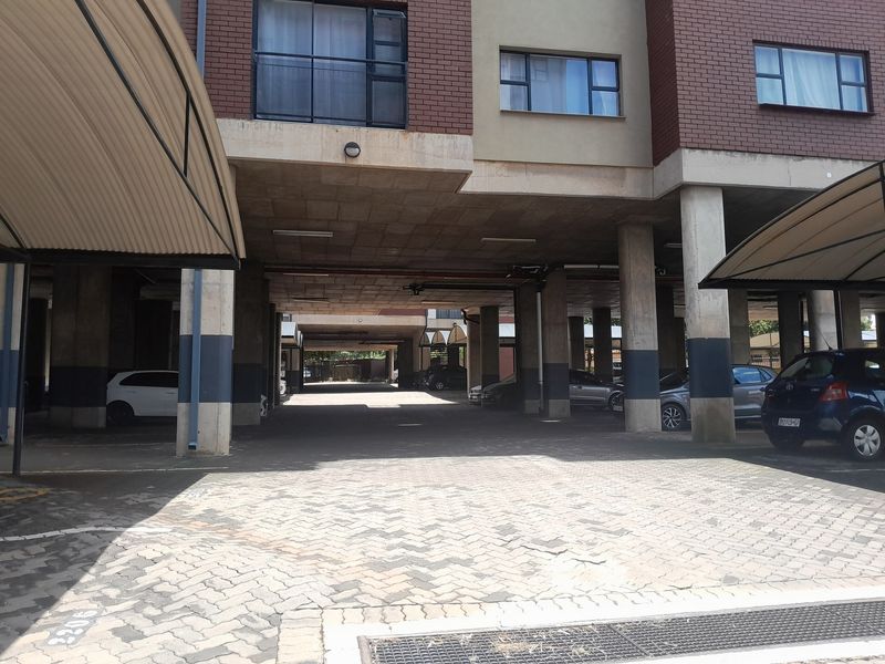 A covered parking area featuring concrete support columns, brick building facade, and paved driveway surface within an apartment complex.