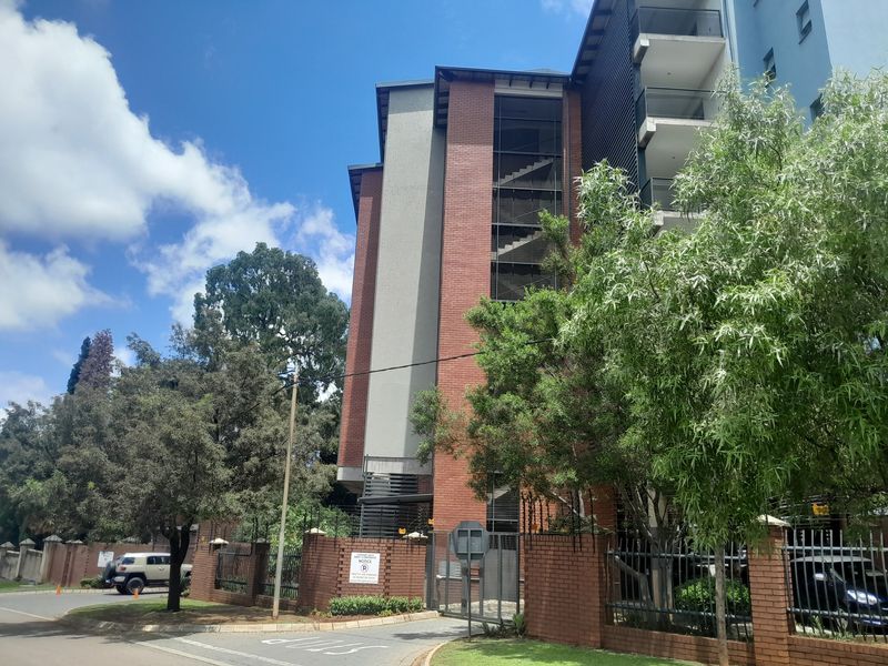 Exterior view of a multi-story apartment building featuring a brick facade, integrated stairwell, and private balconies, secured by a perimeter wall and gate.