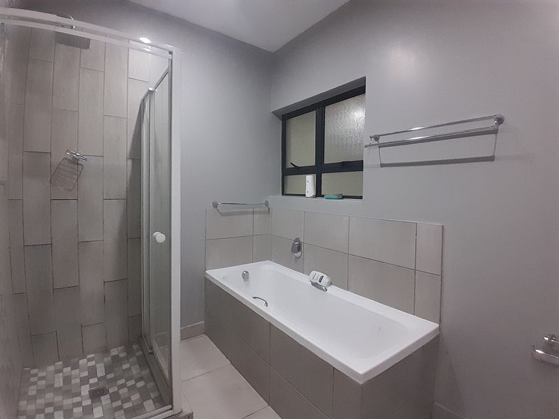 A clean, modern bathroom featuring a separate shower enclosure, a built-in bathtub with tiled surround, and neutral wall finishes.