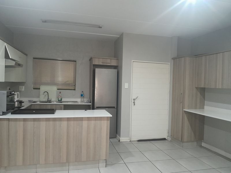 Functional kitchen featuring light wood-look cabinetry, laminate countertops, tiled flooring, and an integrated extractor fan, offering a practical layout for daily use.
