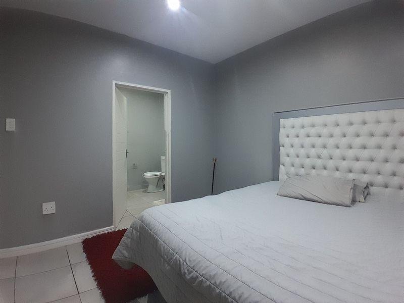 A well-maintained bedroom featuring neutral grey walls, tiled flooring, and direct access to an en-suite bathroom.