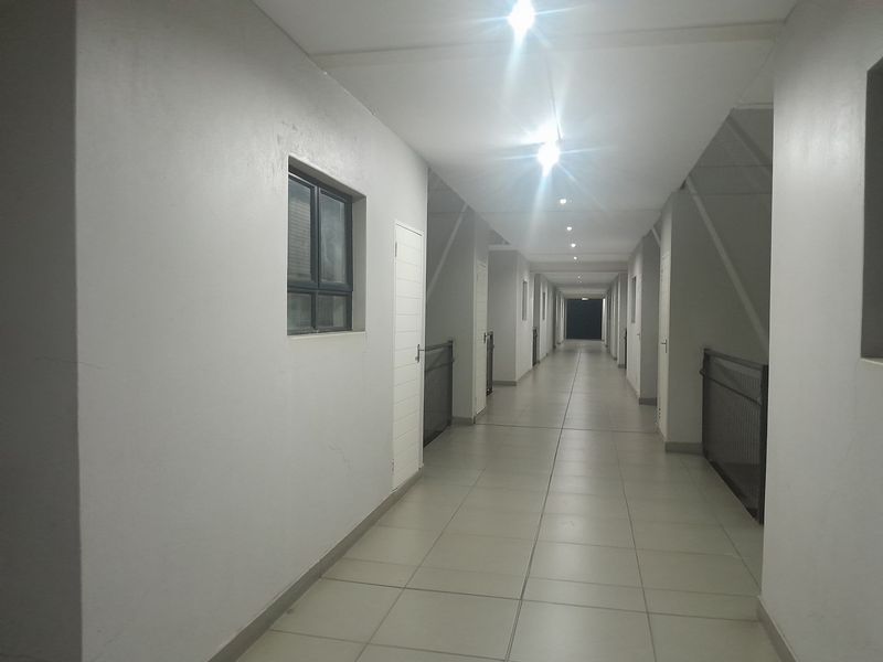 A long, well-lit apartment building hallway featuring tiled flooring and metal safety balustrades.