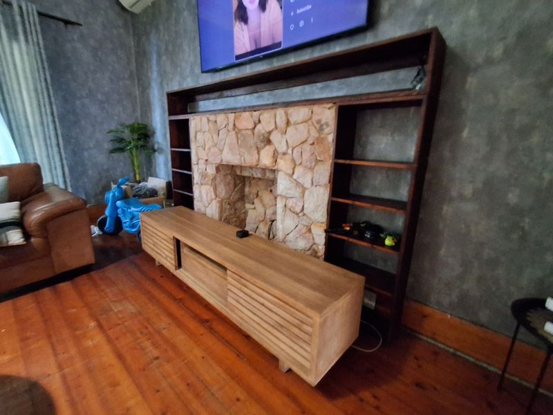 Living room featuring a rustic stone fireplace, integrated timber shelving, and warm timber flooring.