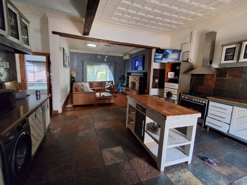 Spacious open-plan living and kitchen area featuring rustic slate flooring, a pressed metal ceiling, exposed timber beams, and a central kitchen island.