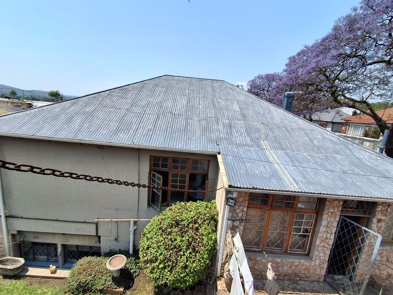Rear elevation of the house featuring a corrugated metal roof, stone cladding accents, and timber-framed windows with security bars.