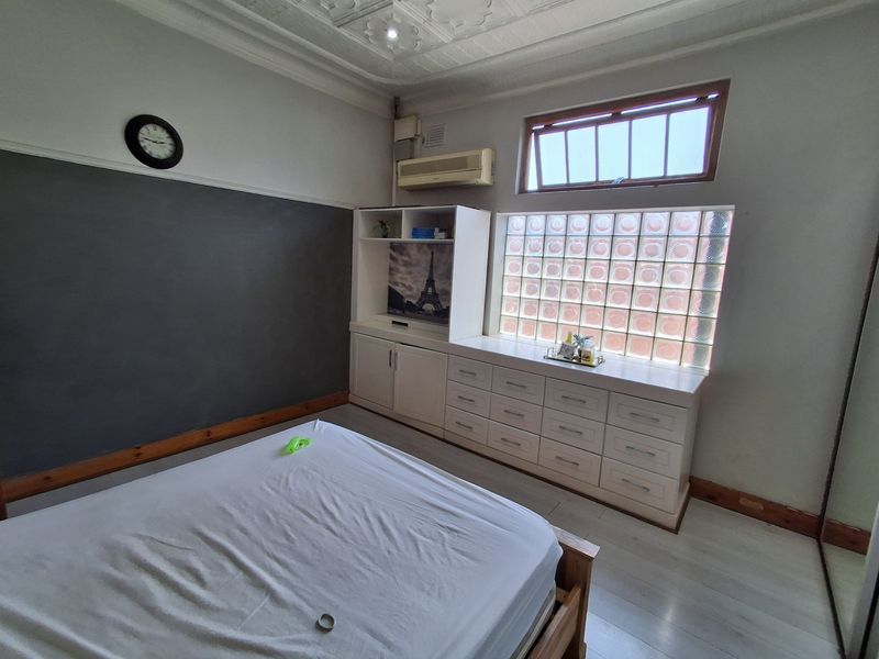 Bedroom featuring built-in cabinetry, a unique glass block window, air conditioning, and decorative ceiling molding with timber skirting boards.