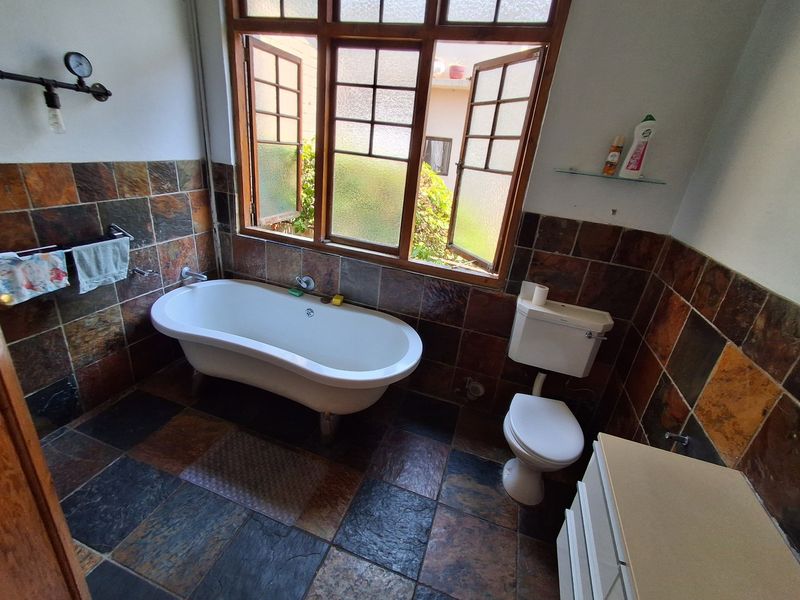 A bathroom featuring a freestanding bathtub, toilet, and vanity cabinet, finished with rustic slate wall and floor tiles and a timber-framed window.