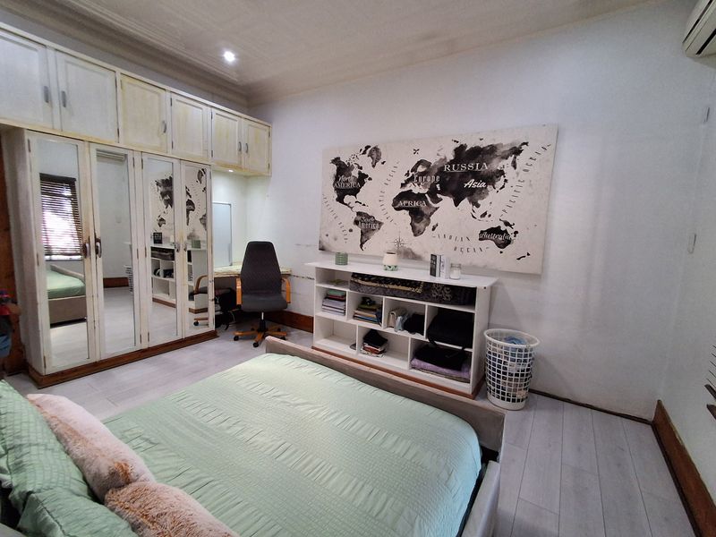 A bedroom featuring extensive built-in cupboards with mirrored doors, laminate flooring, and recessed lighting, offering ample storage space.
