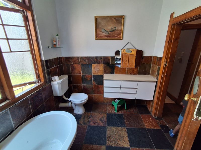 A dated bathroom featuring slate tile flooring and wall cladding, a wall-mounted vanity, and a freestanding bathtub with timber window and door frames.