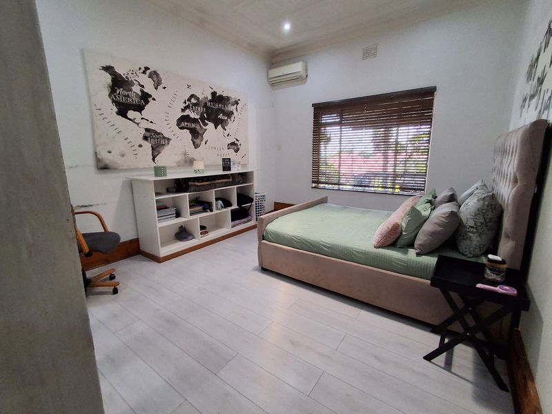 A bedroom featuring light-toned laminate flooring, a wall-mounted split-system air conditioner, and window blinds, offering a functional and neutral living space.