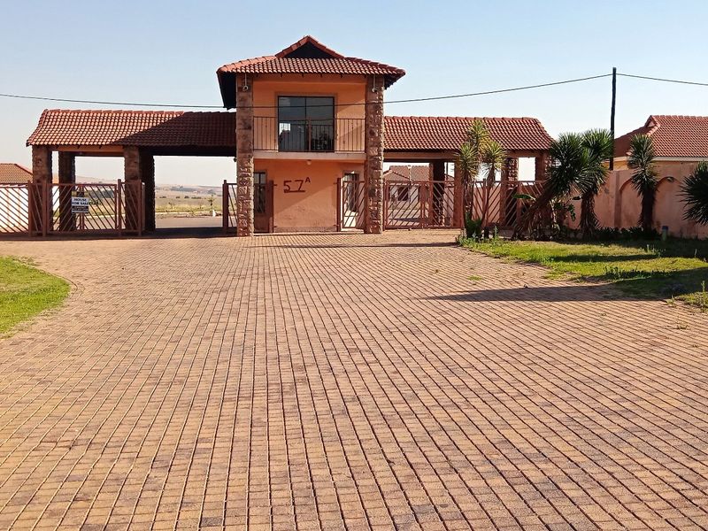 Front view of the townhouse complex entrance featuring a paved driveway, security gatehouse, and perimeter walling.