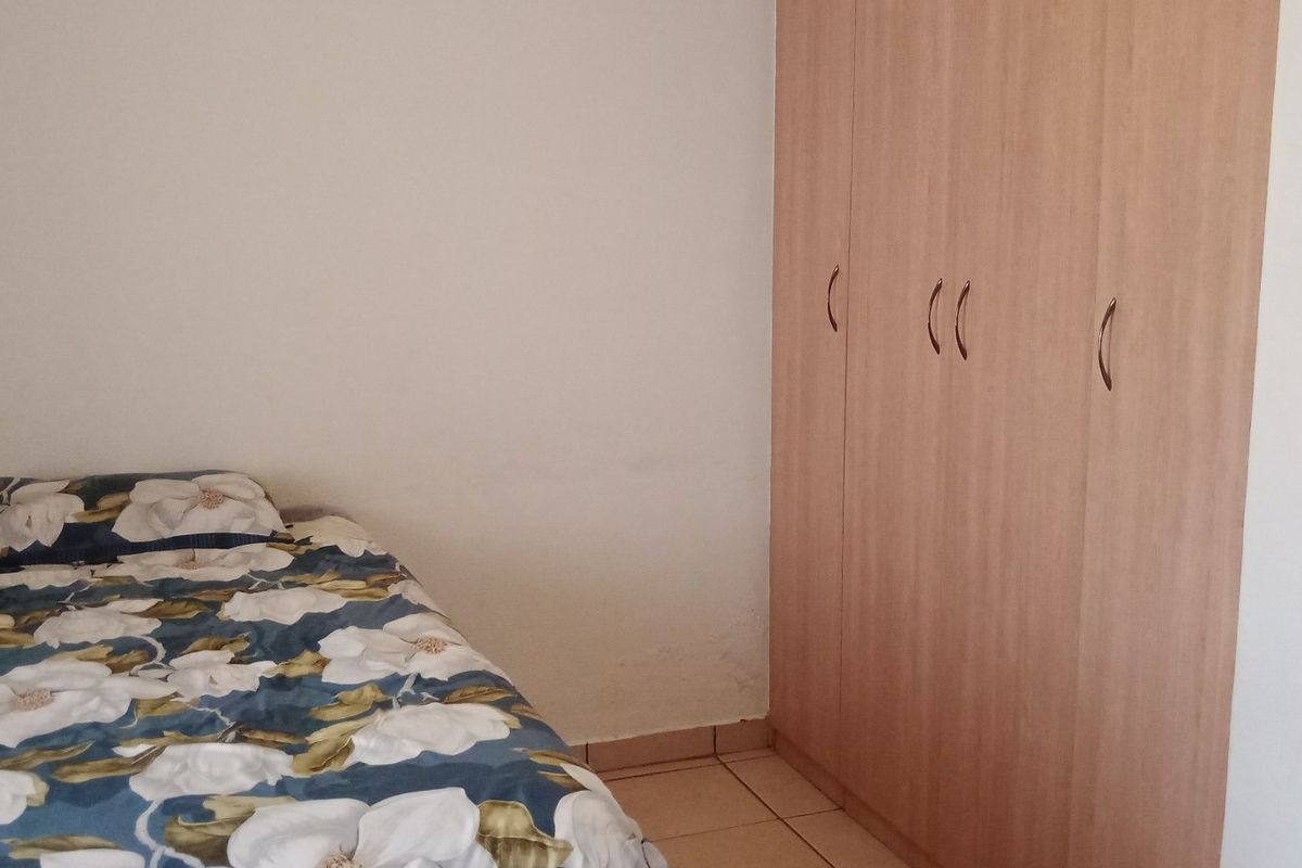 A bedroom featuring light wood-finish built-in wardrobes and tiled flooring.