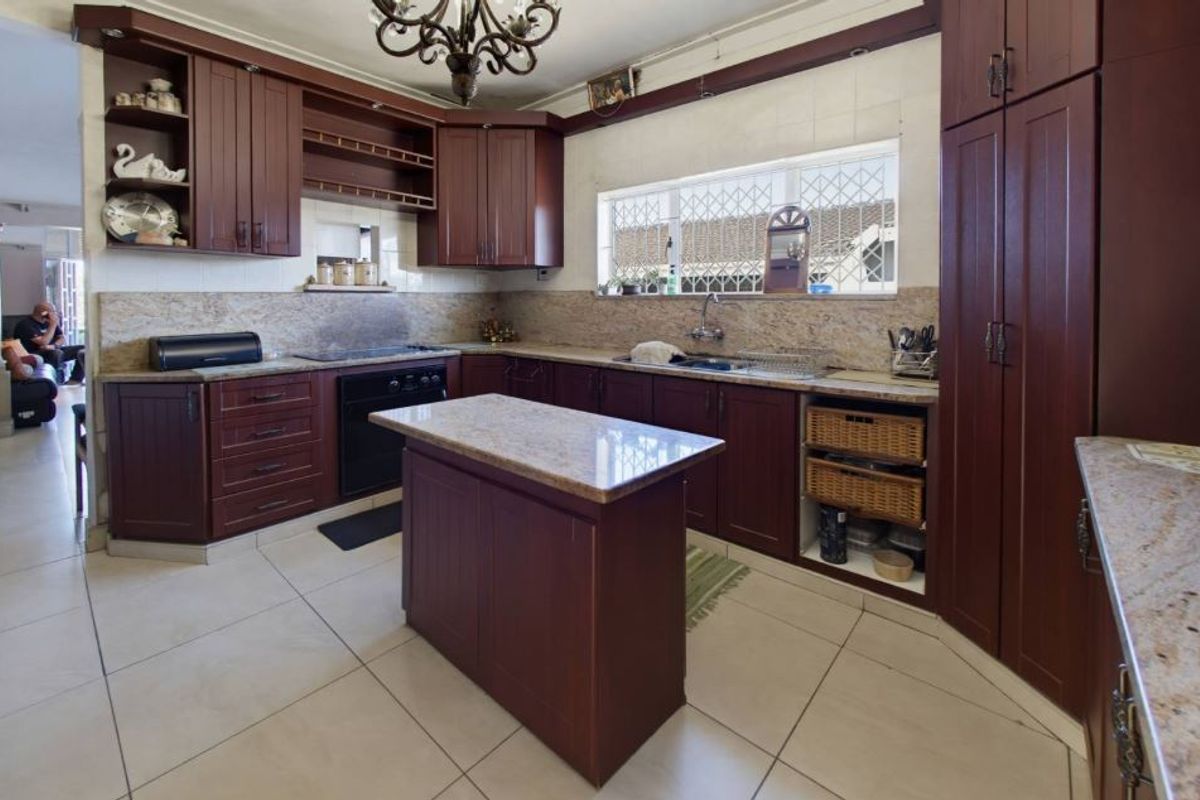 A spacious kitchen featuring dark wood cabinetry, granite countertops, a central island, and tiled flooring, offering a functional layout with ample storage space.