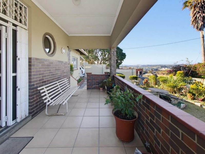 A covered patio featuring tiled flooring, brick wall accents, and a porthole window, offering an elevated view of the surrounding garden and landscape.