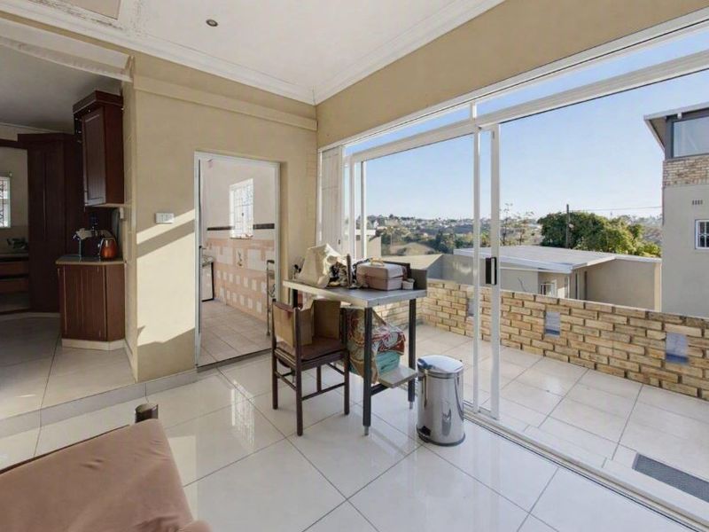 Covered balcony area featuring tiled flooring, brick balustrade, and sliding glass doors, offering an open connection to the adjacent kitchen and interior living space.