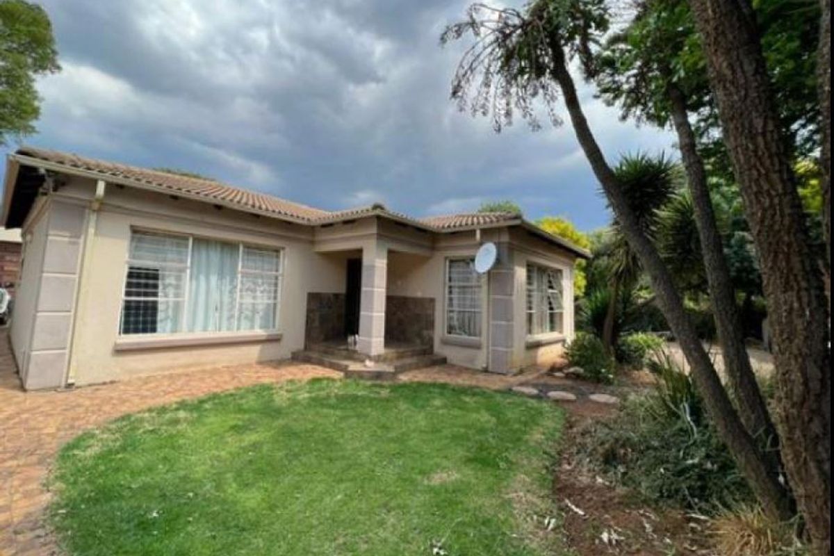 Rear view of a single-story house featuring a tiled roof, plastered walls, paved walkway, and a small garden area.