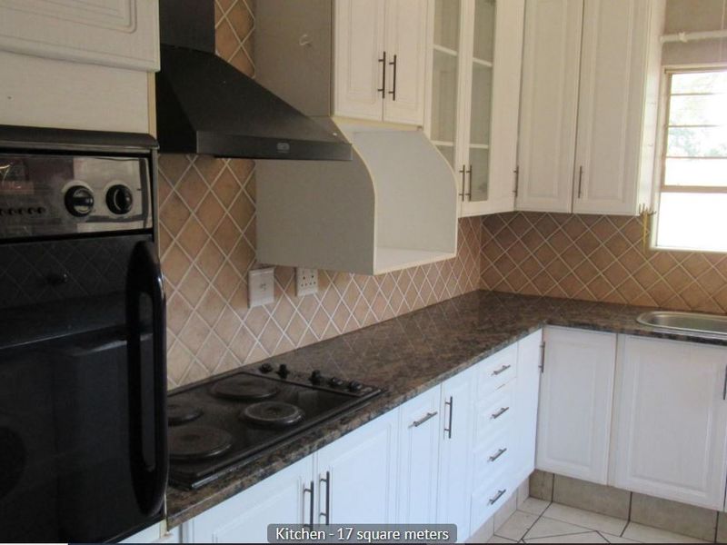 Functional kitchen featuring white cabinetry, dark laminate countertops, built-in oven, electric hob, extractor fan, and a double sink with tiled backsplash.