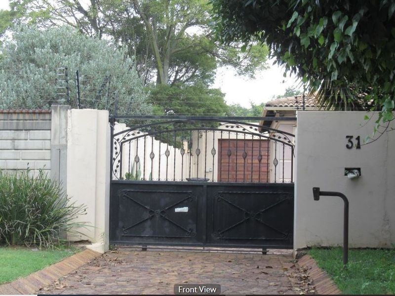 Front entrance view featuring a wrought iron gate, masonry boundary wall with electric fencing, and a paved driveway.